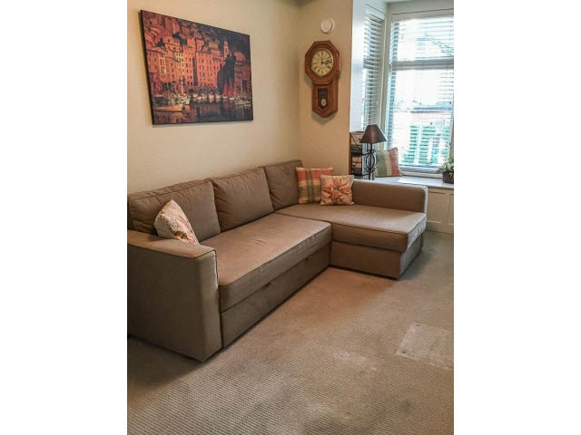 Bright living room with beige sectional sofa, cityscape painting, and bay window with blinds. - 205 - 116 West 23rd, North Vancouver