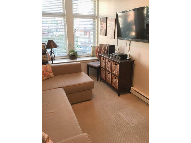 Bright living room with large window, cozy couch, and flat-screen TV. - 205 - 116 West 23rd, North Vancouver