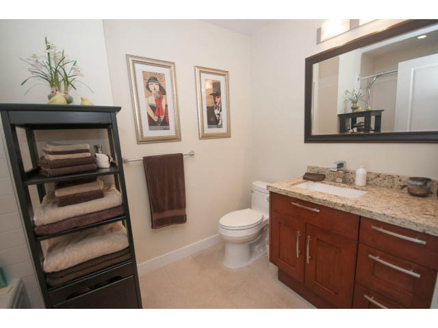 Furnished bathroom with granite countertops, wooden cabinets, and framed artwork. - 205 - 116 West 23rd, North Vancouver