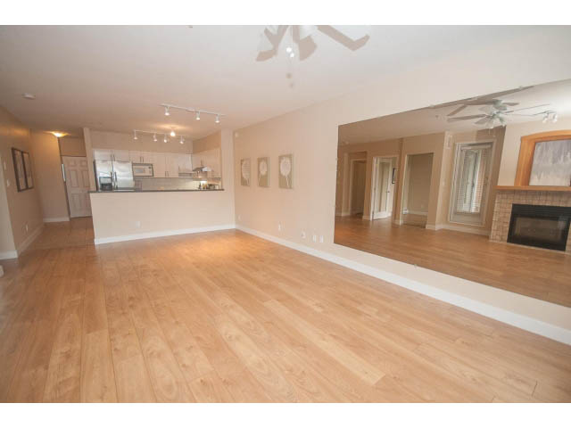 Spacious open-concept living room with hardwood floors and kitchen in the background. - 202 - 3629 Deercrest, North Vancouver