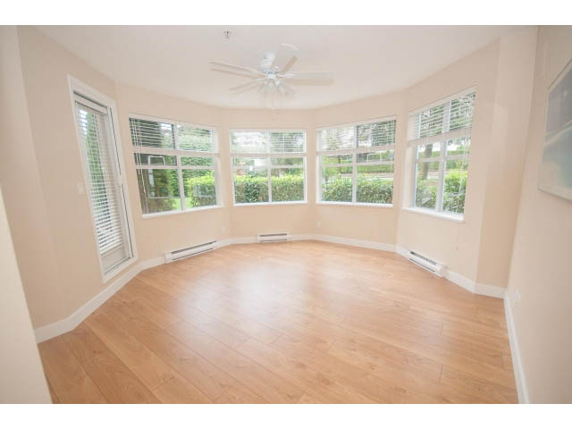 Bright sunroom with hardwood floors and large windows overlooking greenery. - 202 - 3629 Deercrest, North Vancouver