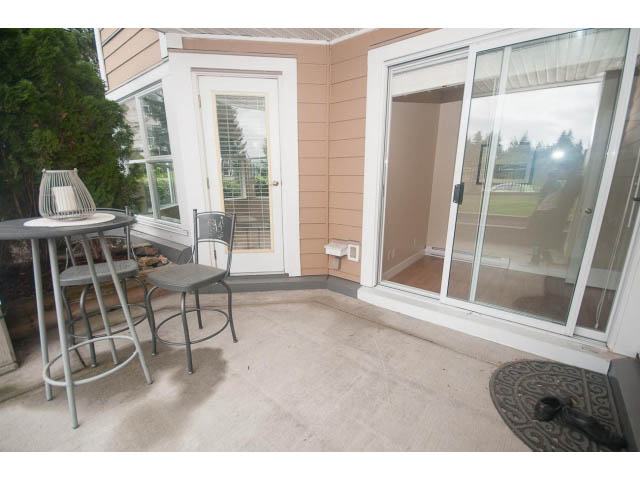 Furnished patio with sliding glass doors, outdoor seating, and a view of greenery. - 202 - 3629 Deercrest, North Vancouver