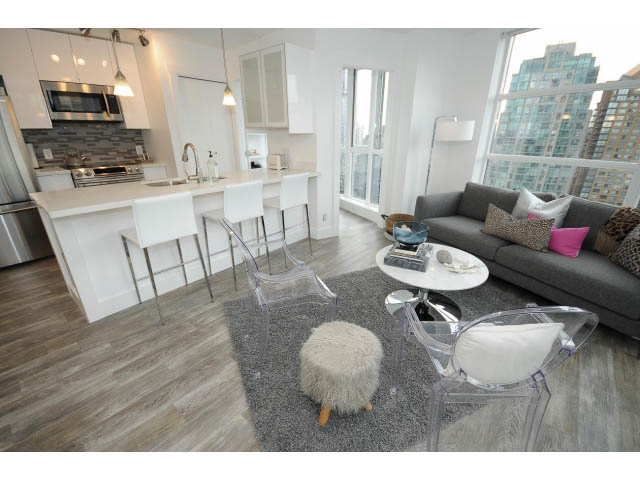 Bright kitchen with white countertops and hardwood floors, open to a modern living area featuring a city view and a cozy...