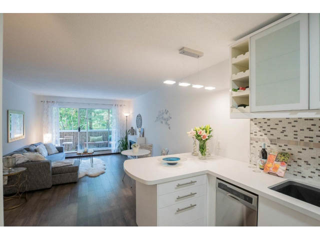 Bright kitchen with white countertops and hardwood floors, leading to a cozy living area with a city view.