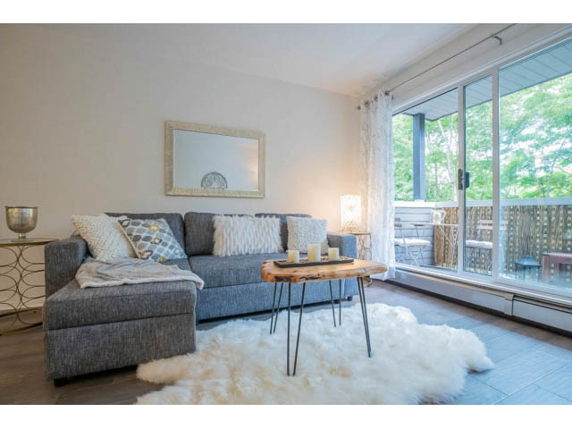 Bright living room with grey sectional, white fur rug, and large window view. - 306 - 570 E 8th Avenue, Vancouver East Side