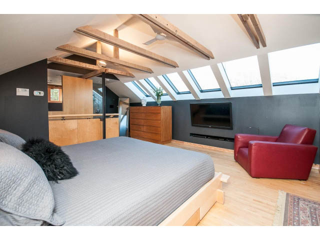 Spacious loft bedroom with wooden beams and skylights, featuring a cozy bed and red armchairs. - 1015 West 16th Ave, Vancouver West Side