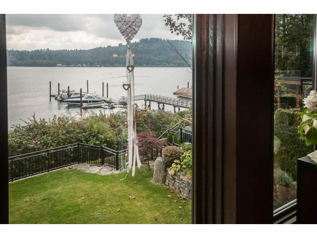 Bright living room with a view of the water and docked boats, surrounded by lush greenery. - 3765 Dollarton Hwy, North Vancouver