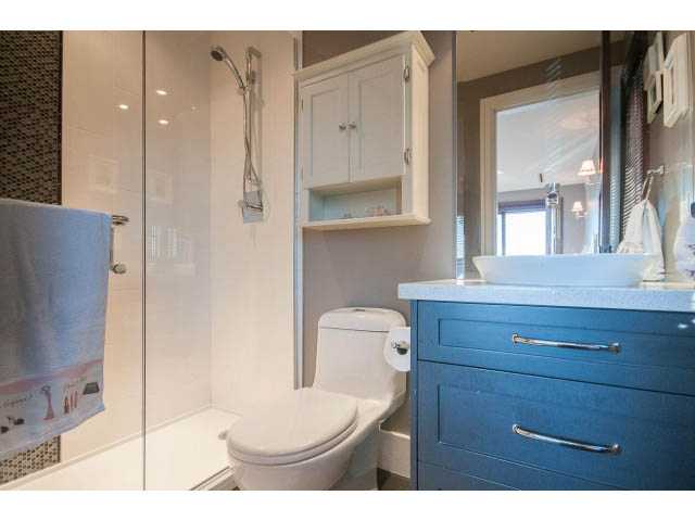 Spacious bathroom with blue cabinets and white fixtures, modern shower setup. - 3765 Dollarton Hwy, North Vancouver