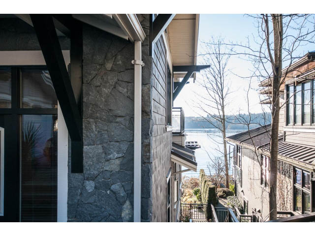 Bright living room with stone walls and large windows, offering a scenic view. - 3765 Dollarton Hwy, North Vancouver