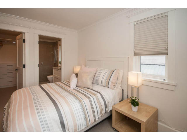Bright bedroom with striped bedding and wooden nightstand, natural light from window. - 1973 W 15th Ave, Vancouver West Side