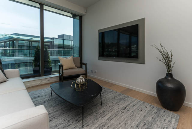 Spacious living room with large windows, modern furniture, and a city view. - 601 - 1355 Bellevue Ave, West Vancouver