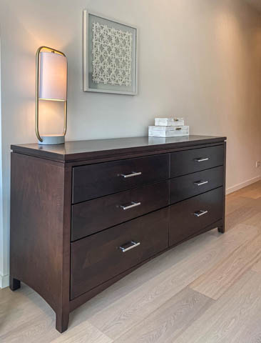 Furnished bedroom with dark wood dresser and modern lamp, hardwood floors. - 601 - 1355 Bellevue Ave, West Vancouver
