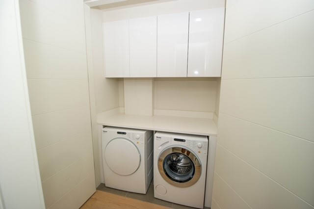 Bright laundry room with white cabinets and stacked washer and dryer. - 601 - 1355 Bellevue Ave, West Vancouver