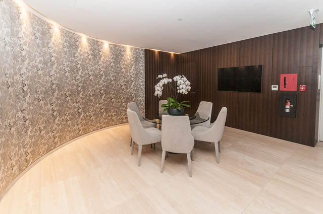 Furnished living room with floral wallpaper, hardwood floors, and a modern TV setup. - 601 - 1355 Bellevue Ave, West Vancouver