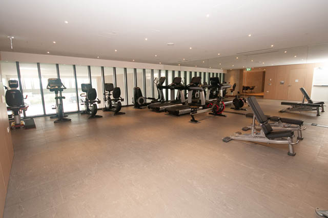 Spacious gym with cardio machines and large windows, light-filled space. - 601 - 1355 Bellevue Ave, West Vancouver