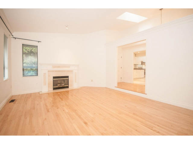 Bright living room with hardwood floors and a fireplace, open to kitchen area. - 4428 Marine Drive, West Vancouver