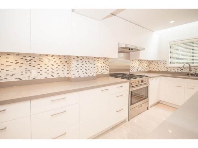 Bright kitchen with white cabinetry, mosaic backsplash, and stainless steel appliances. - 4428 Marine Drive, West Vancouver