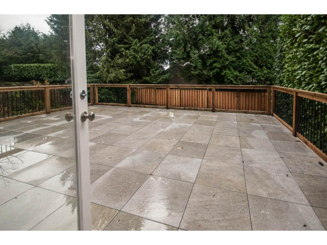 Spacious deck with wooden railing and stone tiles, surrounded by lush greenery. - 4428 Marine Drive, West Vancouver