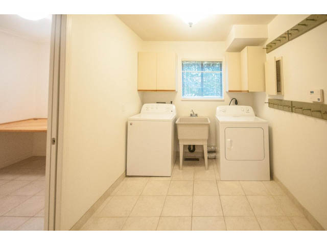 Bright laundry room with white cabinets, tiled floor, and window with blinds. - 4428 Marine Drive, West Vancouver