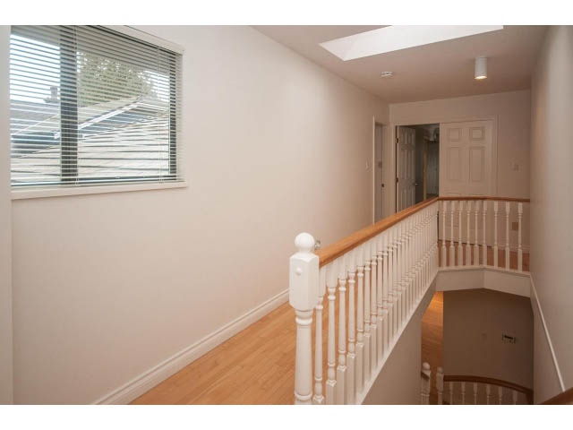 Bright hallway with white railings and hardwood floors, leading to a door and a skylight. - 4428 Marine Drive, West Vancouver
