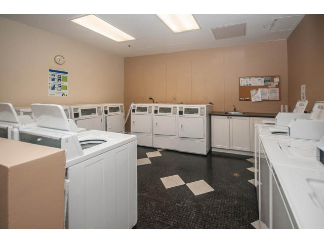 Laundry room with stacked washer and dryer units, beige walls, and a bulletin board. - 1406 - 1060 Alberni Street, Vancouver Downtown