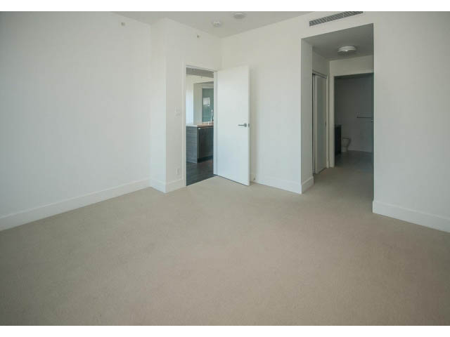 Bright living room with white walls and carpeted floors, leading to a kitchen and bathroom. - 2401 - 1550 Fern Street, North Vancouver
