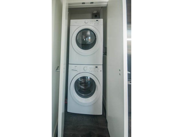 Bright laundry room with stacked washer and dryer, dark flooring. - 2401 - 1550 Fern Street, North Vancouver