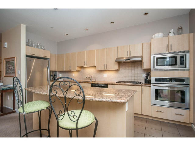 Bright kitchen with granite countertops and stainless steel appliances, featuring a bar area with green cushioned stools.