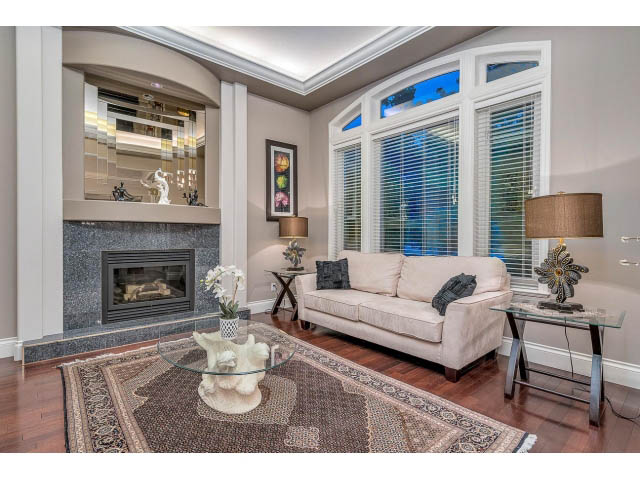 Bright living room with hardwood floors, large windows, and a cozy fireplace. - 4287 Madeley Rd, North Vancouver