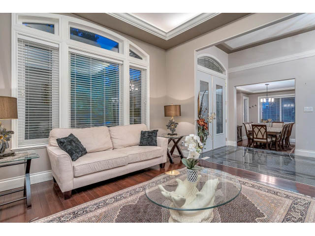Bright living room with hardwood floors, large windows, and a glass coffee table. - 4287 Madeley Rd, North Vancouver