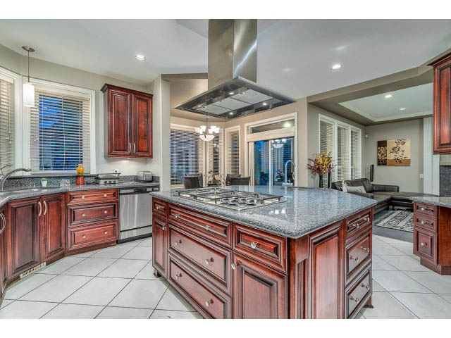 Bright kitchen with dark wood cabinets, granite countertops, and a large island. - 4287 Madeley Rd, North Vancouver