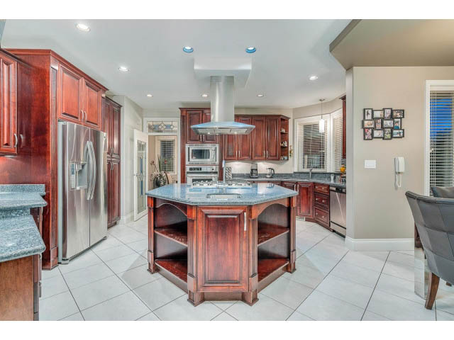 Bright kitchen with dark wood cabinets, granite countertops, and stainless steel appliances. - 4287 Madeley Rd, North Vancouver
