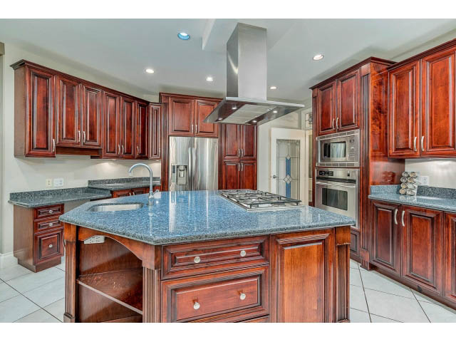 Bright kitchen with dark wood cabinets, granite countertops, and stainless steel appliances. - 4287 Madeley Rd, North Vancouver