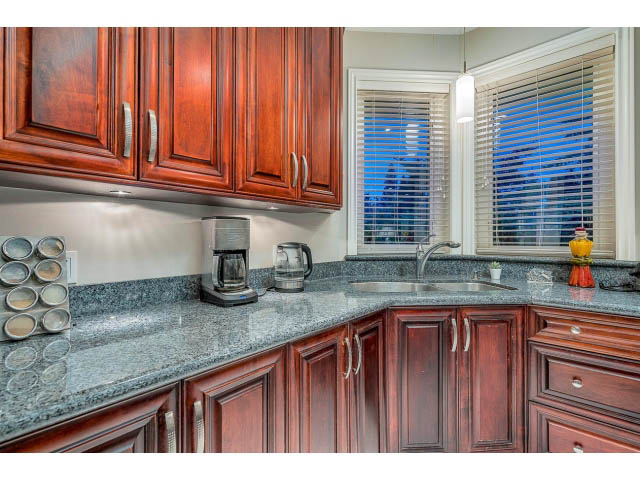 Bright kitchen with granite countertops and dark wood cabinets, featuring a city view through the window. - 4287 Madeley Rd, North Vancouver