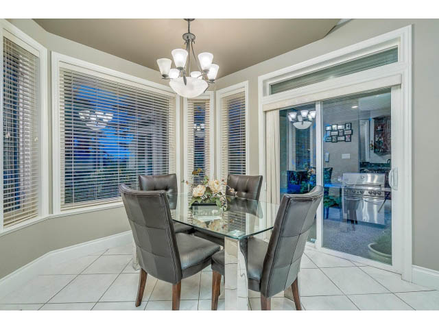 Bright dining area with glass table, modern chairs, and large bay window with blinds. - 4287 Madeley Rd, North Vancouver