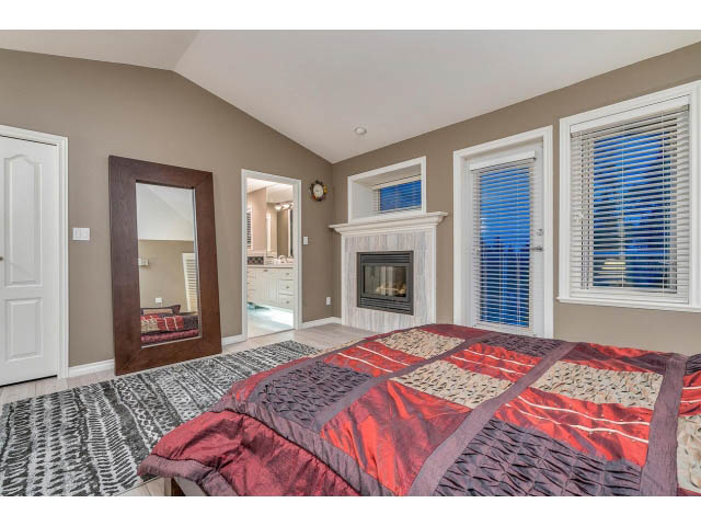 Spacious bedroom with patchwork quilt, large mirror, and window with blinds. - 4287 Madeley Rd, North Vancouver
