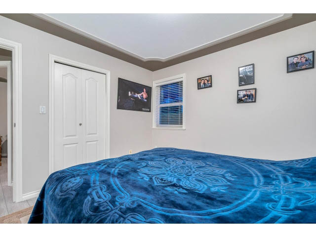 Furnished bedroom with blue patterned bedspread and framed photos on the wall. - 4287 Madeley Rd, North Vancouver
