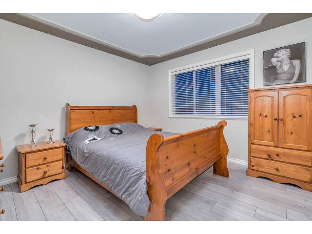 Spacious bedroom with wooden sleigh bed, hardwood floors, and large windows. - 4287 Madeley Rd, North Vancouver