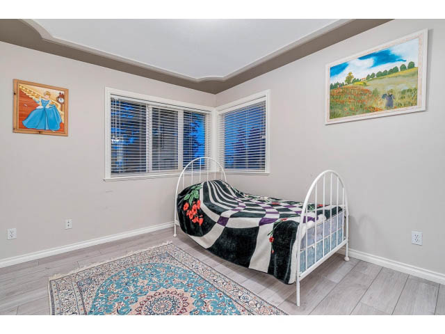 Bright bedroom with two twin beds, patterned bedding, and a colorful rug on hardwood floors. - 4287 Madeley Rd, North Vancouver