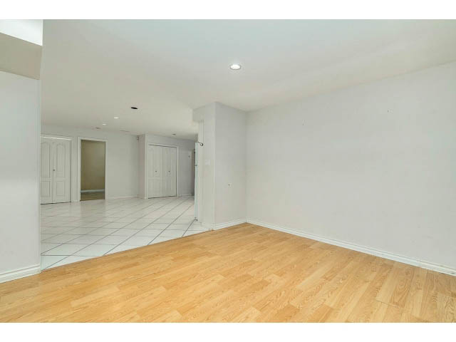 Spacious living room with hardwood floors and white walls, leading to kitchen area. - 4287 Madeley Rd, North Vancouver