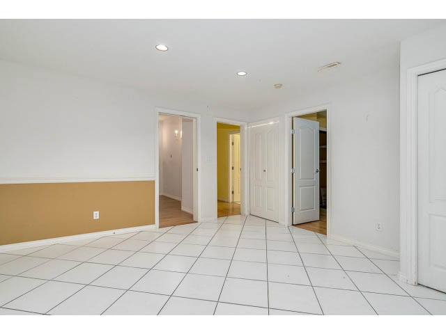 Spacious living room with white walls and tiled floor, leading to another room. - 4287 Madeley Rd, North Vancouver