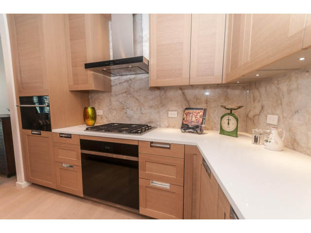 Bright kitchen with light wood cabinets, white countertops, and a marble backsplash. - 409 - 1355 Bellevue Ave, West Vancouver