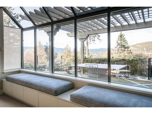 Bright sunroom with large windows, view of mountains and trees, cozy cushioned seating. - 5138 Meadfeild Road, West Vancouver