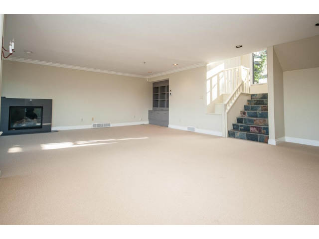 Bright living room with carpeted floors, fireplace, and staircase leading to upper level. - 5138 Meadfeild Road, West Vancouver