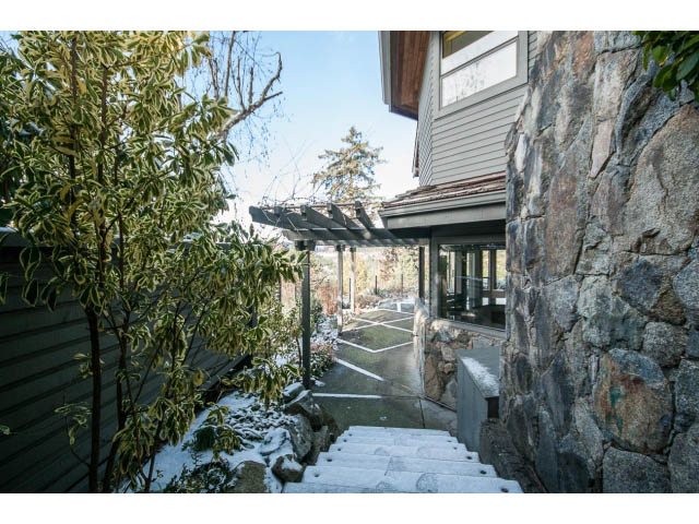Staircase leading to a stone-walled patio, surrounded by greenery and a wooden house. - 5138 Meadfeild Road, West Vancouver