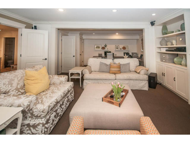 Furnished living room with patterned sofas and a large ottoman, open shelving, and a cozy ambiance. - 840 16th East St, North Vancouver