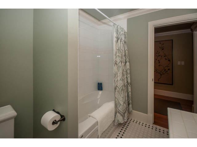 Bathroom with white tiles, patterned shower curtain, and black-and-white floor tiles. - 840 16th East St, North Vancouver