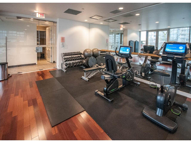 Bright and modern gym with hardwood floors and large windows, featuring cardio machines and weight racks.