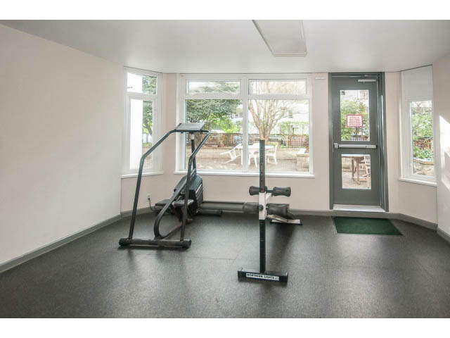 Bright living room with large windows, exercise equipment, and a view of the courtyard. - 108 - 456 Moberly Rd, Vancouver West Side