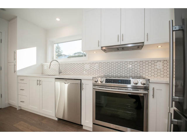 Bright kitchen with white cabinets, hexagonal tile backsplash, stainless steel appliances, hardwood floors, and a window...